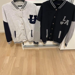 Collegejackor NY - Två snygga collegejackor/koftor i bomull som är NYa men prislappen är borttagen. Sonen har ej använt då de är försmå Ena jackan är ljusgrå med marinblå detaljer och den andra är marinblå med grå ärmar. Båda har randiga muddar, tryckknappar och mjukt bomullsmaterial.