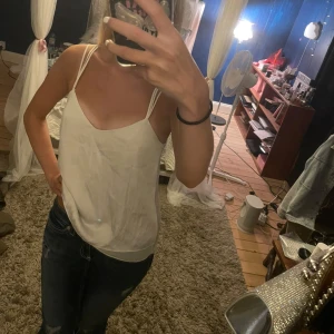 Vit linnetopp med smala axelband - Säljer en vit linnetopp med tunna dubbla axelband och snygg snörning i ryggen, från Kappahl dreams through a lens kollektionen. Toppen har en lös passform och är tillverkad i ett lätt, slätt material som känns svalt mot huden. Perfekt för varma dagar eller när du vill ha en enkel men stilren look.