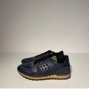 Valentino Rockrunner sneakers blå mocka - Snygga Valentino Rockrunner sneakers i mörkblått skinn och mocka med svarta detaljer och beige sula. Klassiska nitar på sidan och bak, samt mönstrad yttersula. Perfekta för dig som vill ha en lyxig och sportig look.