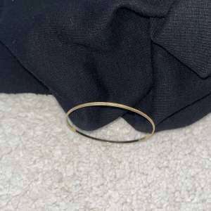 Tunt guldigt armband - Snyggt och enkelt armband i tunn, rund form med guldig finish. Perfekt för dig som gillar minimalistiska smycken med lite extra shine. Armbandet är slätt och har en diskret textur som ger det en cool touch. Passar till alla outfits och är lätt att matcha med andra smycken.
