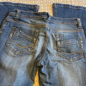 Blå bootcut jeans Dorothy Perkins - Snygga blå bootcut jeans från Dorothy Perkins med klassiska fickor bak och fram, samt detaljerade sömmar. Jeansen har dragkedja och knapp framtill och är tillverkade i mjukt denimtyg med lätt slitning för en cool look. Storlek xs/s o passar lite kortare människor 
