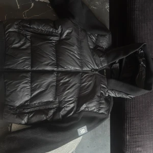 Svart puffercardigan från BVALDI - Snygg svart pufferjacka från BVALDI i storlek M. Jackan har quiltad design, dragkedja framtill och två fickor med dragkedja. Ärmar och huva är i stickat material för extra komfort och stil. Perfekt för kalla dagar när du vill hålla stilen. nypris=2500 priset är ej hugget i sten skick 9/10 den är som ny