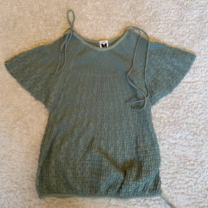 Grön glittrig topp från Missoni - Supersnygg grön topp från Missoni med glittrigt material och strukturmönster. Toppen har korta vida ärmar och knytband vid axlarna för en unik look. Perfekt för dig som vill sticka ut med en cool och trendig stil.