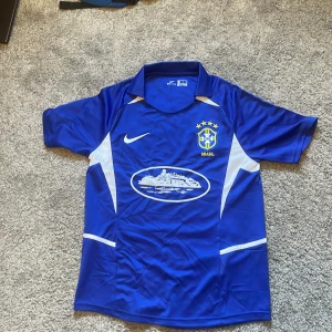 Blå Brasil Nike fotbollströja S - Säljer en blå Brasil fotbollströja från Nike i storlek S. Tröjan har korta ärmar, vit detalj på sidorna och broderat CBF-emblem med fyra gula stjärnor. Materialet är lätt och andas, Dri-Fit polyester. Perfekt för dig som älskar fotboll och vill sticka ut på planen.