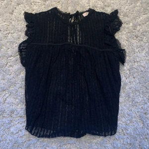Svart spetsblus med volang från Nelly - Supersöt svart blus från Nelly i spets med volangdetaljer på axlarna och knytning i nacken. Blusen är ärmlös och har en lätt transparent känsla med fina ränder i tyget. Kontakta mig här på plick im man har mer frågor eller om man vill ha mer bilder! Köparen står för kostnaden av frakten💗💐🌺