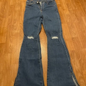 Blå bootcut jeans med slitningar - Snygga blå jeans med bootcut-modell och slitna detaljer vid knäna. Jeansen har klassisk femficksdesign och är tillverkade i jeansmaterial. Perfekta för en avslappnad och trendig look.