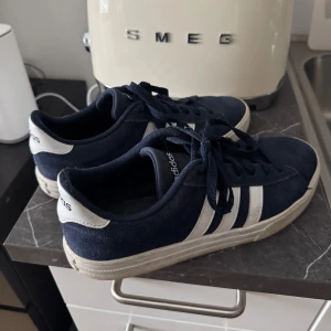 Adidas sneakers i marinblå mocka - Säljer ett par klassiska Adidas sneakers i marinblå mocka med vita detaljer och de ikoniska tre ränderna på sidorna. Skorna har snörning och vit sula, perfekt för dig som gillar en stilren och sportig look. Storlek 40 (US 7,5).