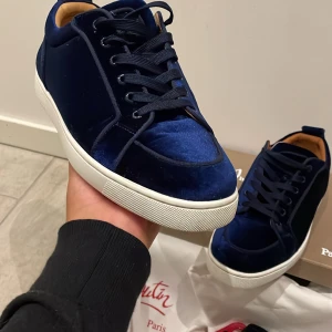 Christian Louboutin - Säljer ett par riktigt snygga sneakers från Christian Louboutin i mörkblå sammet med vita sulor och svarta snören. Insidan är i beige skinn och de har en klassisk rund tå. Kommer med originalpåse, extra skosnören och skohorn.                   Modellen är navy velvet en exklusiv modell är inte säljs längre