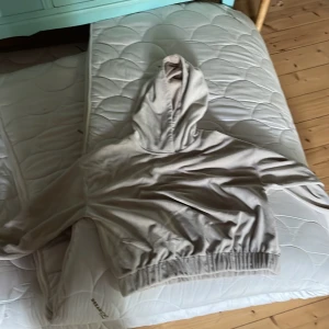 Beige hoodie med brodyr från Lindex - Beige hoodie från Lindex med broderad text 'New Day' framtill och små glittriga detaljer. Tröjan har luva, långa ärmar och resår i midjan och vid ärmsluten. Perfekt för en chill och avslappnad stil.