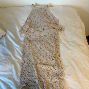 Beige stickad kjol & topp med volang - Säljer en beige stickad topp & kjol med snyggt hålmönster och volangdetalj längst ner. settet är ärmlös och har en hög hals, vilket ger en cool och modern vibe. Perfekt för sommarens alla tillfällen när du vill vara både bekväm och trendig.