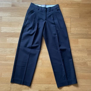 Svarta lågmidjade kostymbyxor från JJXX - Snygga svarta kostymbyxor från JJXX med klassisk rak passform och pressveck framtill. Byxorna har låg midja och bälteshällor, vilket gör dem perfekta för en clean och stilren look. Materialet känns mjukt och har en lätt glansig finish.