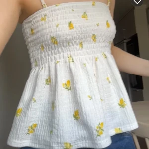 Vit blommig bandeau tubtopp - Supersöt bandeau tubtopp i vit med små gula blommor från Gina. Toppen har smock upptill🌼Man kan ta av banden om man vill det, och även ha den med banden! Säljer för att den är lite för liten på mig🌷