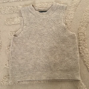 Beige stickad väst från Vero Moda - Stickad väst i beige från Vero Moda i storlek XS. Modellen är ärmlös med ribbad struktur och rund halsringning. Perfekt att slänga över en skjorta eller t-shirt för en chill lager-på-lager-look.