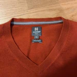 Orange  kashmirtröja från Manor - Snygg rostbrun tröja från Manor i 100% kashmir. V-ringad modell med ribbade muddar och lång ärm. Perfekt för dig som gillar en klassisk och stilren look med extra mjuk känsla.