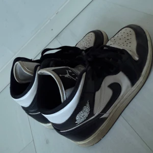 Nike Air Jordan 1 svart/vit 37,5 - Säljer ett par klassiska Nike Air Jordan 1 i svart och vitt. Skorna har hög modell med snörning, svart swoosh och Air Jordan-logga på sidan. Tillverkade i skinn med perforerad tå och svartvit yttersula. Perfekta för dig som gillar streetstyle och sneakers med ikonisk design. Köpt på Jd sports 