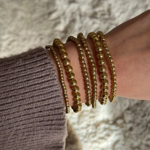 6 Guldiga pärlarmband  - Säljer ett set med guldiga armband i flera lager, gjorda av små och stora runda pärlor.