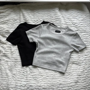 2-pack Even&Odd toppar - Två stycken magtröjor/crop-tops i färgerna svart o grå. Stretchigt material och formar sig väldigt fint på kroppen.