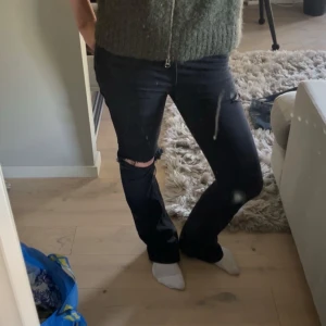 Svarta bootcut jeans med slitningar - Säljer ett par svarta jeans med bootcut-modell och snygga slitningar vid knäet, även ett litet hål på övre låret och på bakfickan. 