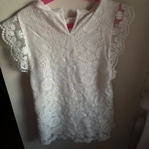 Vit spetsblus från Pieces XS - Supersöt vit blus från Pieces i storlek XS, helt täckt av detaljerad spets med blommönster. Blusen har ärmlös design med vackra spetsvolanger vid axlarna och liten knapp i nacken. Använd fåtal gånger inga defekter😍 läs gärna bio🥰 OBS! Skriv innan köp, säljer på fler ställen❤️