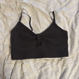 Svart ribbad linnetopp Tally Weijl - Svart ribbad linnetopp från Tally Weijl med smala axelband och en snygg knutdetalj framtill. Toppen är croppad och har en enkel, stilren look som passar perfekt till jeans eller kjol. Mjuk och stretchig för en bekväm passform.