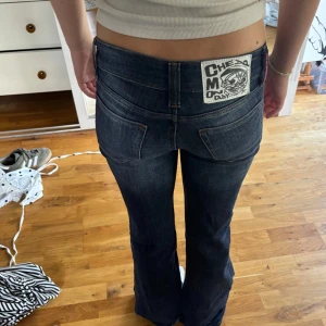 Cheep monday jeans  - Snygga mörkblå jeans med bootcut passform och coolt tryck på bakfickan. Jeansen har klassisk femficksdesign, låg midja och är urtvättad för en trendig look. Storlek 26/30. Lite slitna nere vid fötterna. 