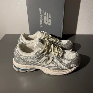new balance 1906r silver metallic sea salt - Säljer ett par New Balance 1906R sneakers i vitt med silverdetaljer och mesh-överdel. Skorna har snörning, platt sula och rund tå. Märkets ikoniska N-logga på sidan och coola detaljer i syntet och mesh gör dem riktigt fräscha och trendiga.