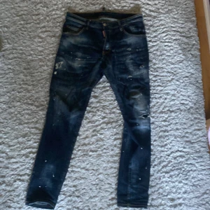 Mörkblå skinny jeans från Dsquared2 - Snygga mörkblå skinny jeans från Dsquared2 med slitna detaljer och färgstänk för en cool, edgy look. Klassisk femficksmodell med Dsquared2-logga på bakfickan och röd etikett vid fickan fram. Jeansen har kontrastsömmar och är tillverkade i stretchig denim.