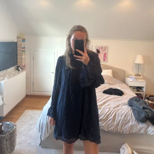 Marinblå prickig klänning & Other Stories - Säljer en marinblå kortklänning från & Other Stories Paris Atelier med vita prickar. Klänningen har långärmade, lätt puffade ärmar och hög hals med smockdetaljer. Använd få gånger💕