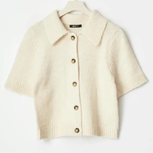 Beige stickad T-shirt  - Superfin beige stickad kofta från Gina Tricot med korta ärmar och stora knappar framtill. Koftan har en klassisk krage och ribbade kanter som ger en snygg och trendig look. Perfekt att styla med jeans eller kjol för en chill vibe.