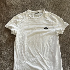 Vit barn t-shirt från J.Lindeberg i L - Vit t-shirt från J.Lindeberg med svart logotyp på bröstet. Klassisk rund halsringning och korta ärmar. Perfekt basplagg med stilren design och mjukt material.