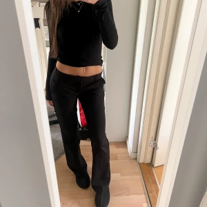 Svarta kostymbyxor med bootcut - Snygga svarta kostymbyxor med bootcut passform och låg midja. Byxorna har klassisk design med diskret dragkedja och raka ben som blir vidare nertill. Perfekta för en stilren och trendig look. Ord pris: 499