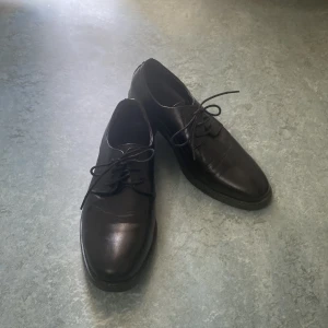 Svarta skinnloafers med snörning - Klassiska svarta loafers i skinn med rund tå och snörning. Perfekta för en stilren look och passar till både kostym och mer avslappnade outfits. Snygg och tidlös design.