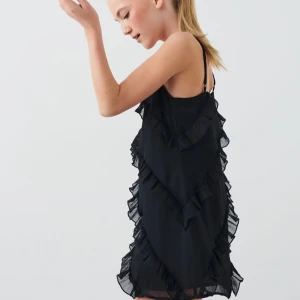 Svart klänning med volanger - Snygg svart klänning med volanger och smala axelband. Perfekt för en kväll ute eller en speciell tillställning. Klänningen har en luftig passform och är tillverkad i ett lätt material.