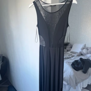 Svart långklänning med meshdetaljer från Sisters Point - Säljer en svart långklänning från Sisters Point i storlek XS. Klänningen har meshdetaljer upptill och vid midjan som ger en snygg kontrast. Ärmlös modell med rund halsringning och figurnära passform upptill.