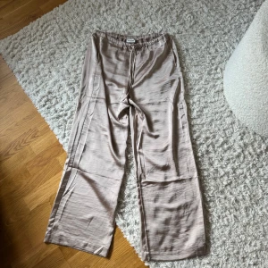 Beige satinbyxor  - Säljer ett par jätte fina beigea byxor i satin med raka ben och snöre i midjan. Använda 1 gång.
