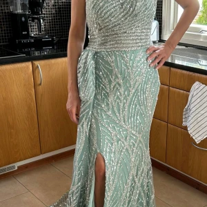 Mintgrön glittrig långklänning med slits - Säljer en mintgrön långklänning med glittriga paljetter och ett elegant mönster. Klänningen har en axel och en hög slits framtill, samt en vacker drapering vid midjan. Perfekt för bal eller fest! 💎