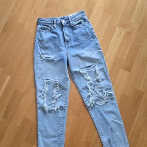 Ljusblå mom jeans med stora slitningar från H&M - Ljusblå mom jeans från H&M med ultra high waist och stora slitningar på båda benen. Klassisk femficksmodell med dragkedja och knapp. Perfekta för en avslappnad och trendig look.