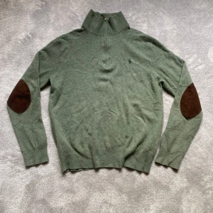 Grön halvzip tröja från Polo Ralph Lauren - Snygg grön stickad tröja från Polo Ralph Lauren med halv dragkedja och bruna mockadetaljer på armbågarna. Normal i storleken📏 enda defekt är ett knappt synligt hål på ryggen (se sista bilden) hör av er vid frågor eller mått