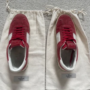  Valentino Flycrew  - Säljer ett par snygga Valentino sneakers i rött och vitt med klassisk design. Skorna har röd mocka, vita skinnpaneler och röda skosnören. Perfekta för dig som vill sticka ut med stilrena och exklusiva sneakers. Skorna är i ett använt skick men fortfarande mycket kvar att ge alla nitar är kvar och mockan är bra. Kom pm för frågor och Funderingar. Skorna är i storlek 39 men passar 40-40,5.