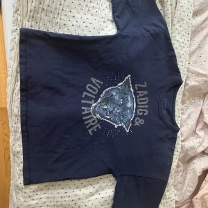 Svart t-shirt med pantermotiv från  Zadig & Voltaire - Cool svart t-shirt från Zadig & Voltaire med stort tryck av en panter och text framtill. T-shirten har rund halsringning och är dekorerad med små nitar runt motivet. passar många storlekar.