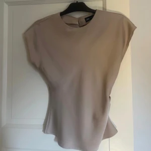 Beige satinblus från Zara - Säljer en stilren beige blus från Zara i satinliknande material. Blusen har korta ärmar, rund halsringning och knappdetalj i nacken. Perfekt för dig som gillar en enkel men elegant look.💗 använd vid ett tillfälle 