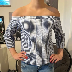 Randig offshoulder blus - Säljer en blåvit randig offshoulder blus med trekvartsärm. Blusen har en rak passform och är perfekt för vår och sommar. Snygg till både jeans och kjol!