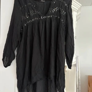 Svart blus med paljettdetaljer från KappAhl - Svart blus från KappAhl med långa ärmar och v-ringning. Blusen har glittriga paljettdetaljer upptill och ett luftigt, lätt tyg som faller snyggt. Perfekt för dig som vill ha något stilrent med lite extra bling. Mellan L - XL