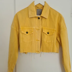 Gul croppad jeansjacka från Vero Moda - Säljer en croppad gul jeansjacka från Vero Moda i storlek XS. Jackan har klassisk krage, två bröstfickor med knappar och rå kant nertill. 