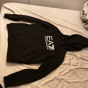 Svart hoodie från Emporio Armani - Säljer en snygg svart hoodie från Emporio Armani, EA7. Den är i bra skick och perfekt för både vardag och chill. Hoodien har en stor logga på framsidan och är gjord i ett mjukt material som känns skönt mot huden. Passar perfekt till höst och vinter!