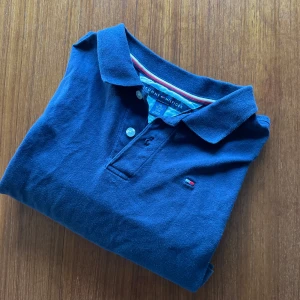 Mörkblå Tommy Hilfiger piké - Mörkblå piké från Tommy Hilfiger. Perfekt för sommaren. Skicket är 8/10 pågrund av att dem är lite syda vid sidorna men det syns ej. Pikén funkar på folk som är ca 160cm. 