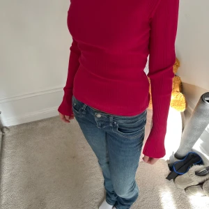 Ribbad röd långärmad topp - Säljer en snygg ribbad röd långärmad topp med figurnära passform.. Toppen har rund halsringning och är gjord i ett stretchigt material som sitter bekvämt.