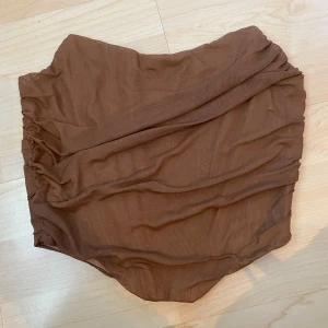 Brun ”korsett”-topp med dragkedja - Säljer en brun korsett-topp med dragkedja baktill. Toppen har rynkade detaljer och är axelbandslös.