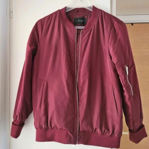 Vinröd bomberjacka  - Säljer denna vinröda bomberjacka från Vila. Den är i bra skick utan några defekter. Supersnygg nu till våren!