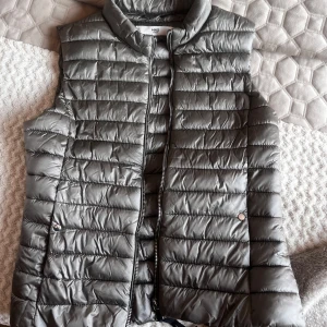 Grå dunväst från MNG Casual - Snygg grå dunväst från MNG Casual med ståkrage och dragkedja framtill. .